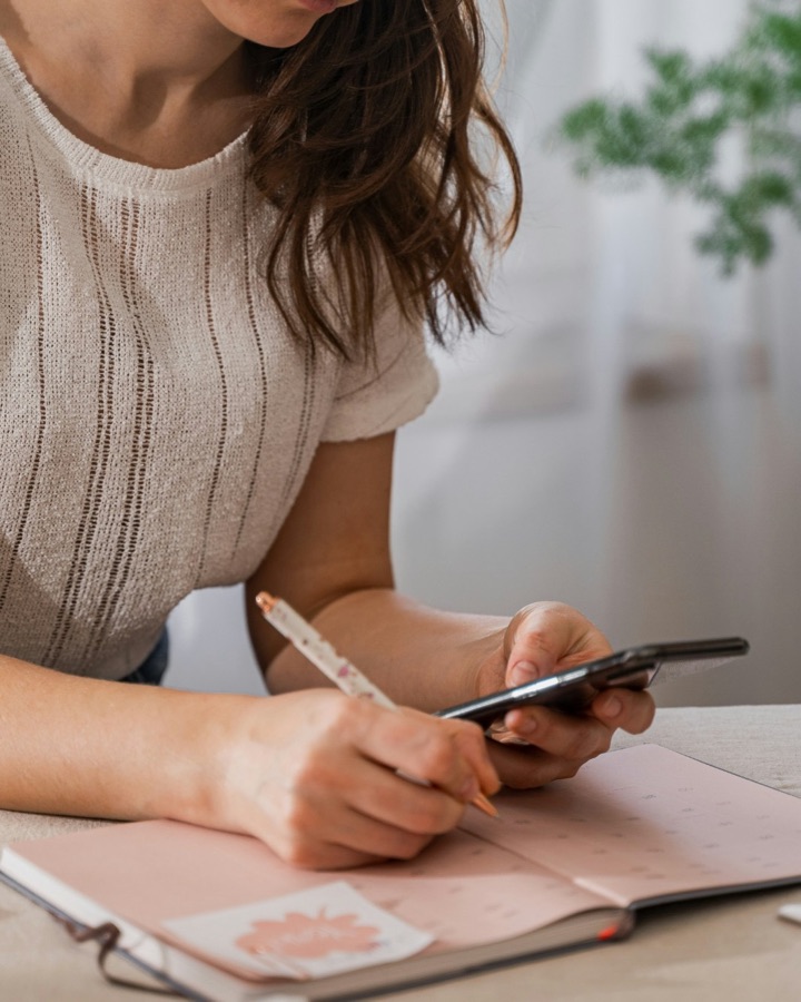 Une femme note une question dans son carnet, téléphone en main